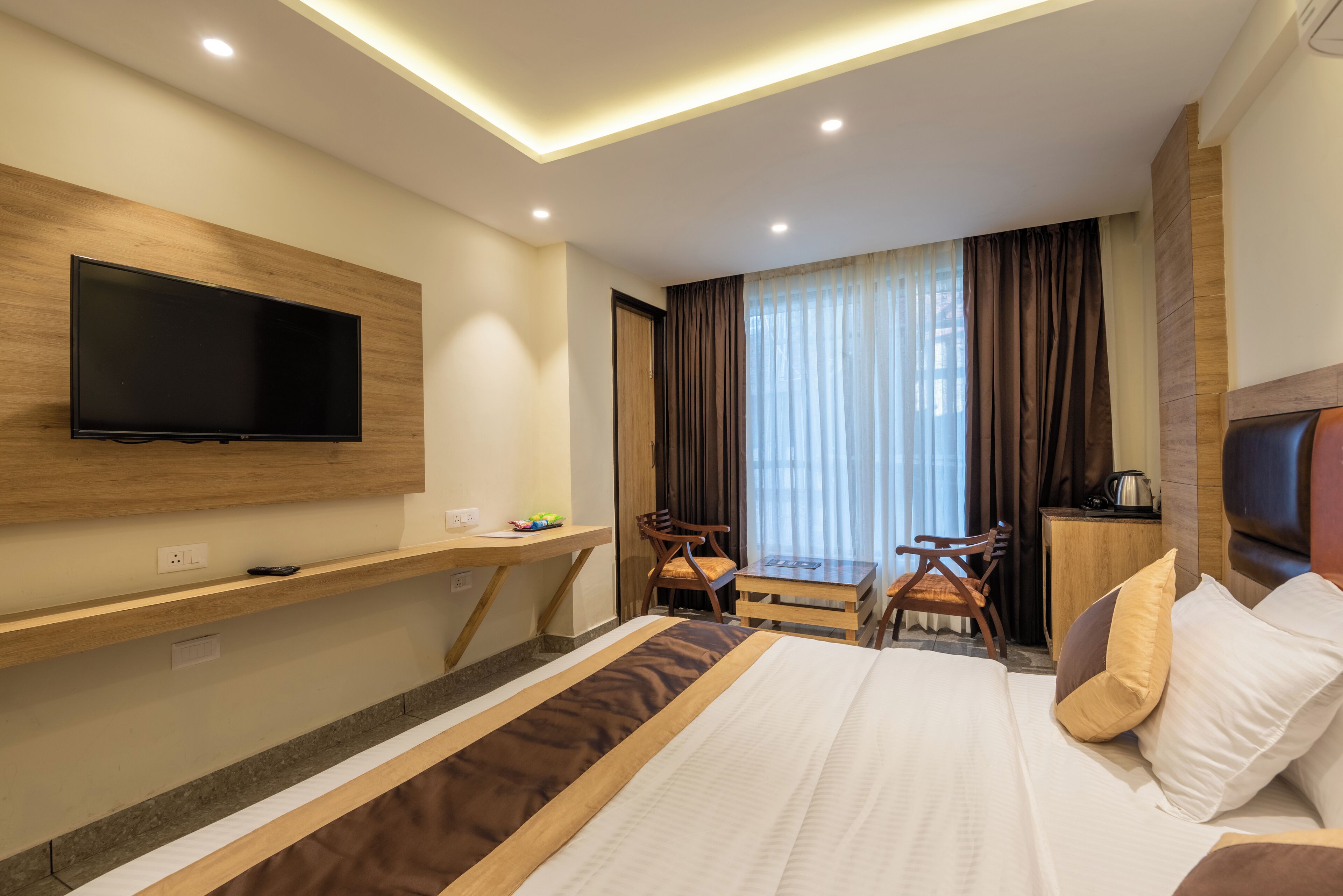 Habitación de hotel con cama, escritorio, televisión y ventana con cortinas.