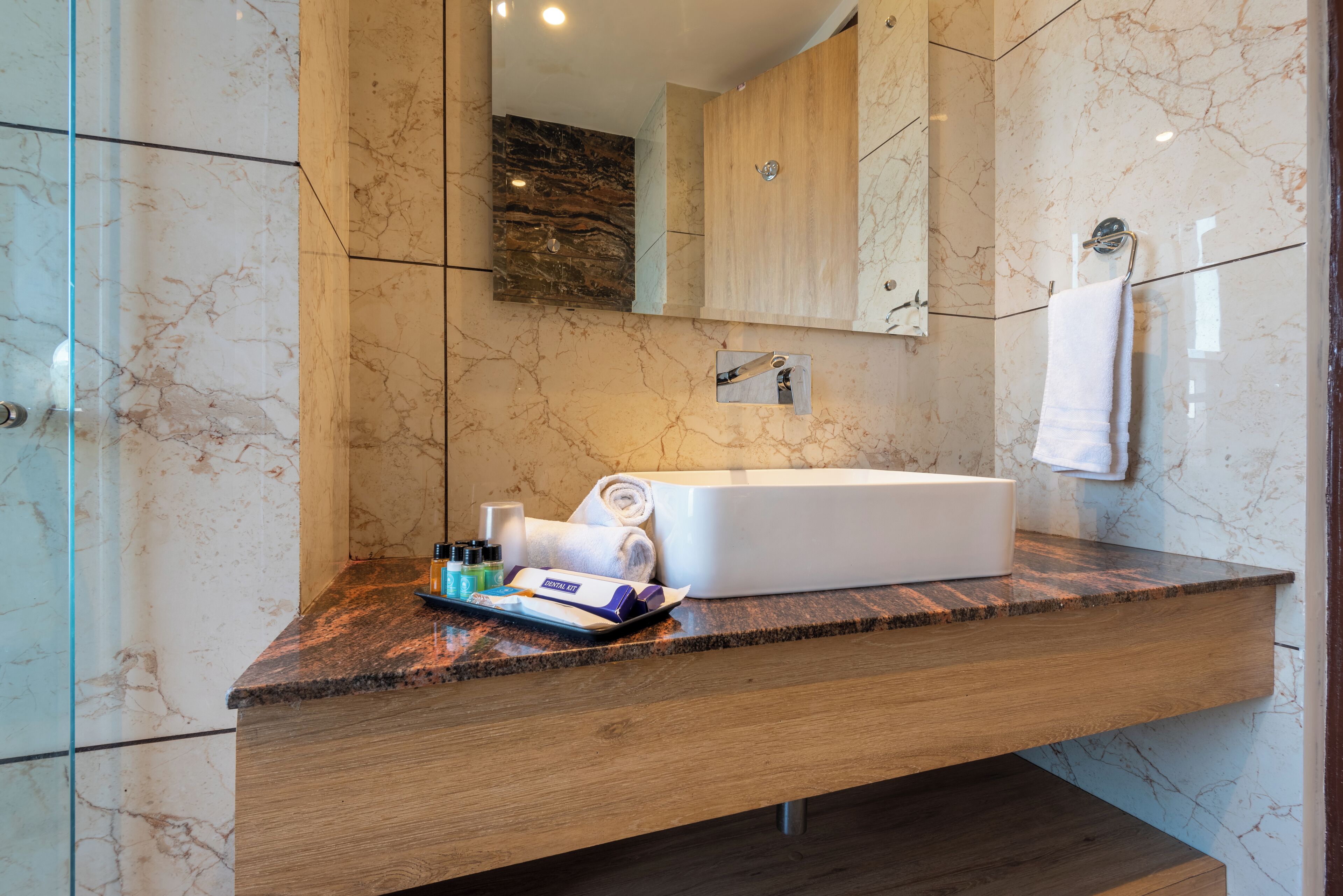 Une salle de bain moderne avec un mur recouvert de carreaux de marbre, un meuble-lavabo en bois, une baignoire blanche et un porte-serviettes.