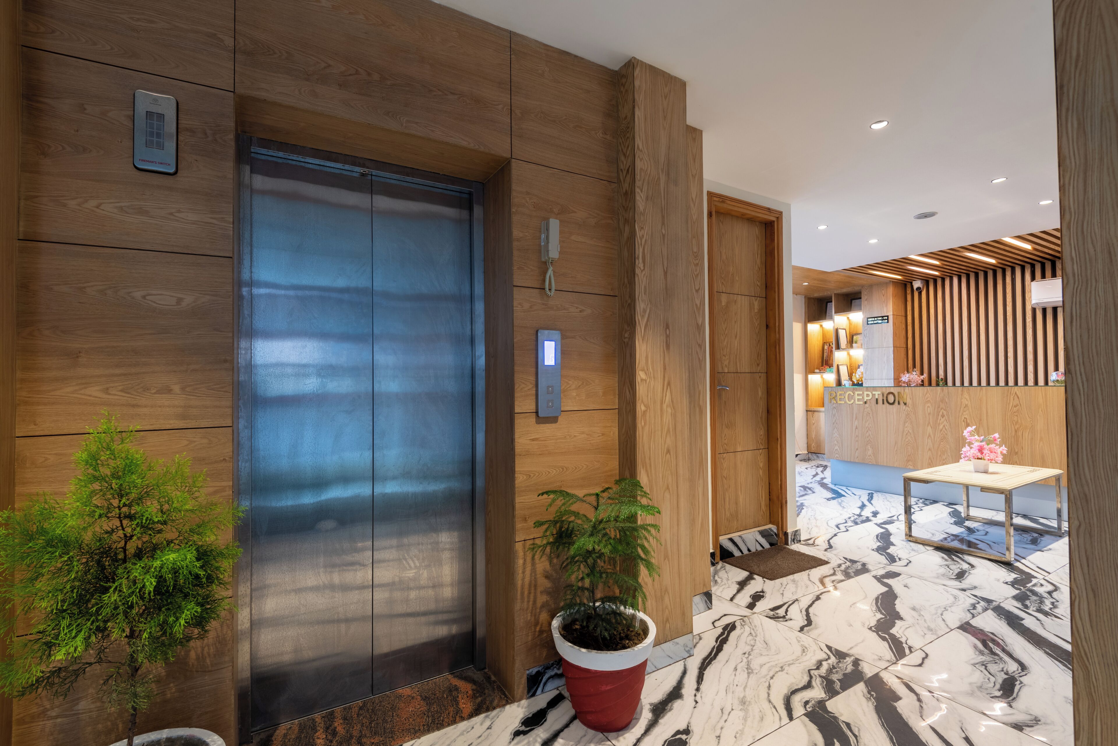 Un área de recepción moderna con mostrador, pared de madera, planta en maceta y suelo de mármol.