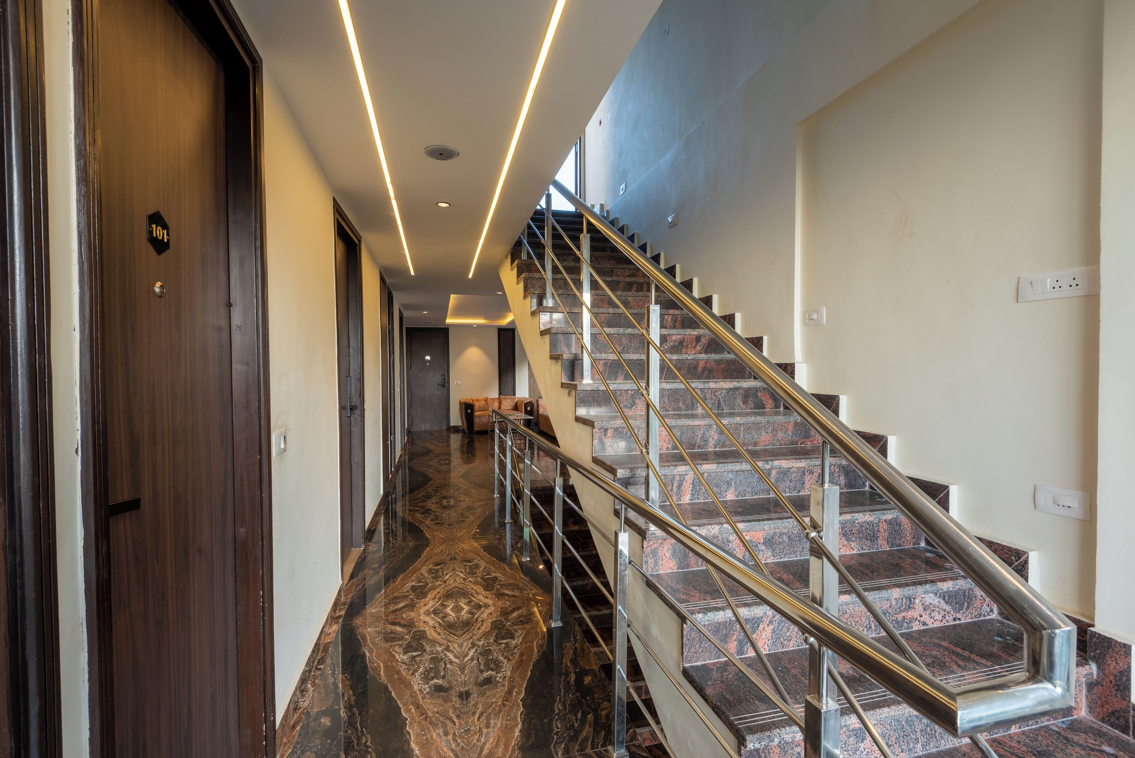 A modern hotel corridor with a marble floor, a wooden door labeled "101", and a staircase with metal railings.