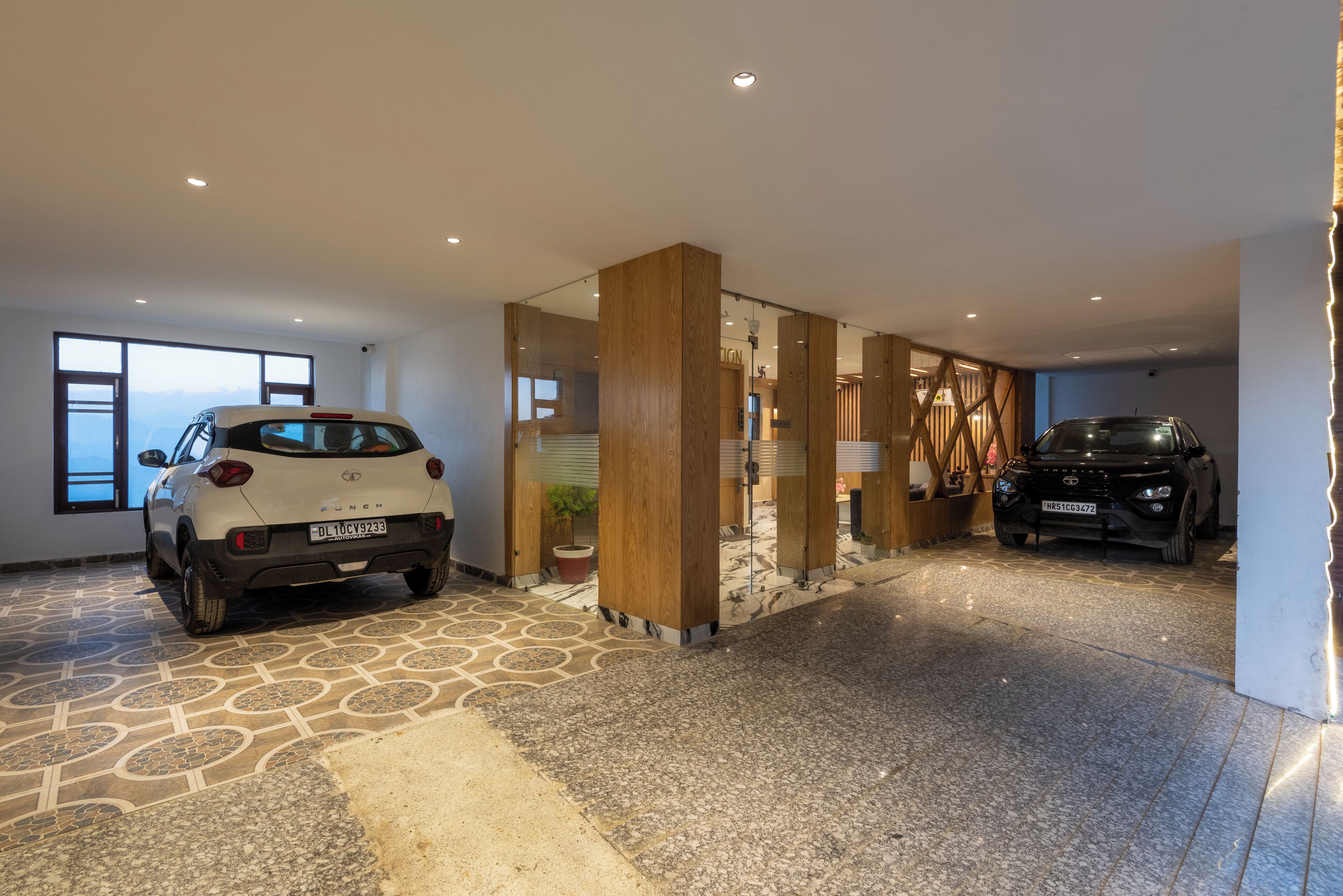 Un garaje espacioso con dos coches aparcados, suelo con estampado de piedra y un panel de madera.