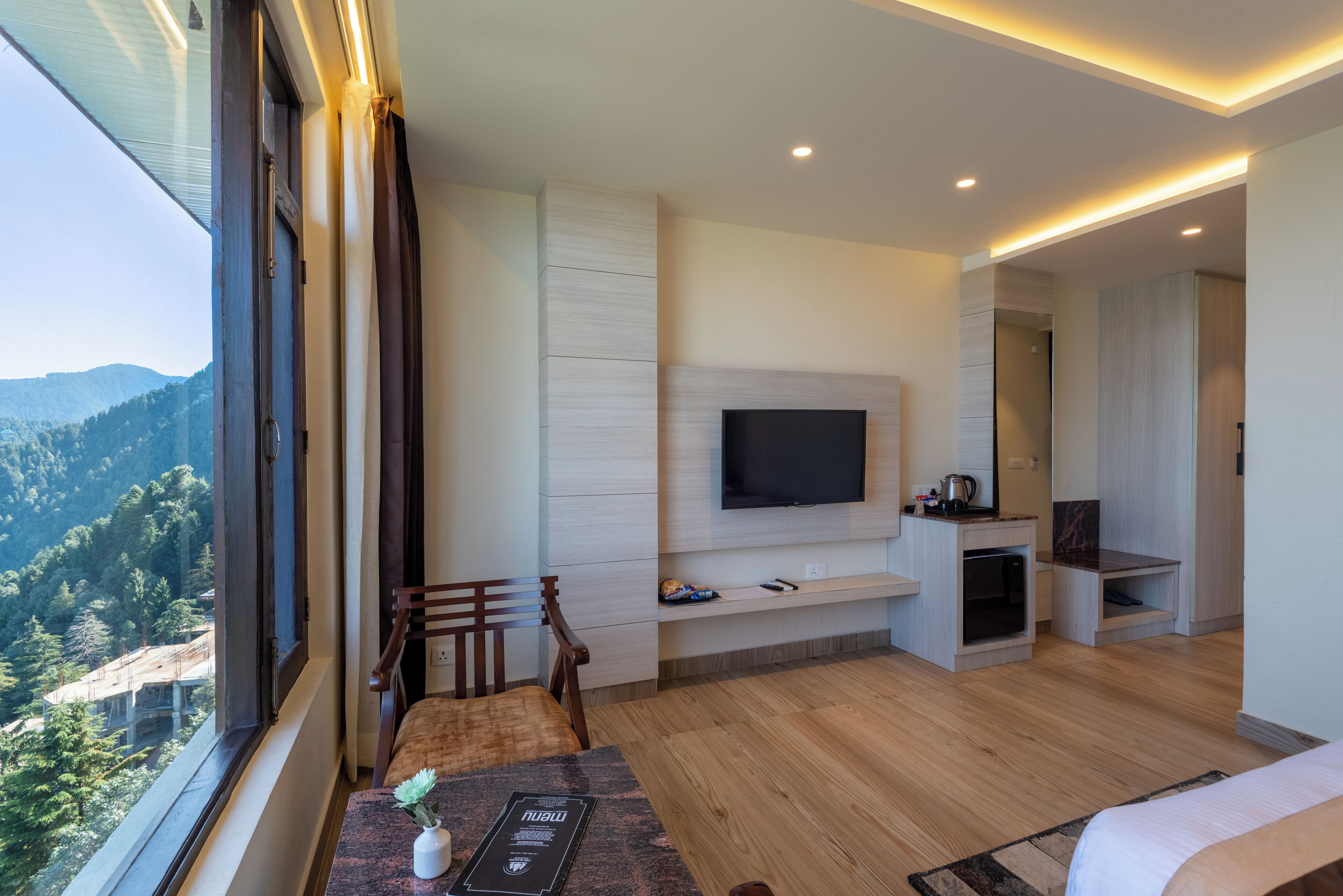 A modern room with a large window, a flat-screen TV, wooden flooring, and a dining area.
