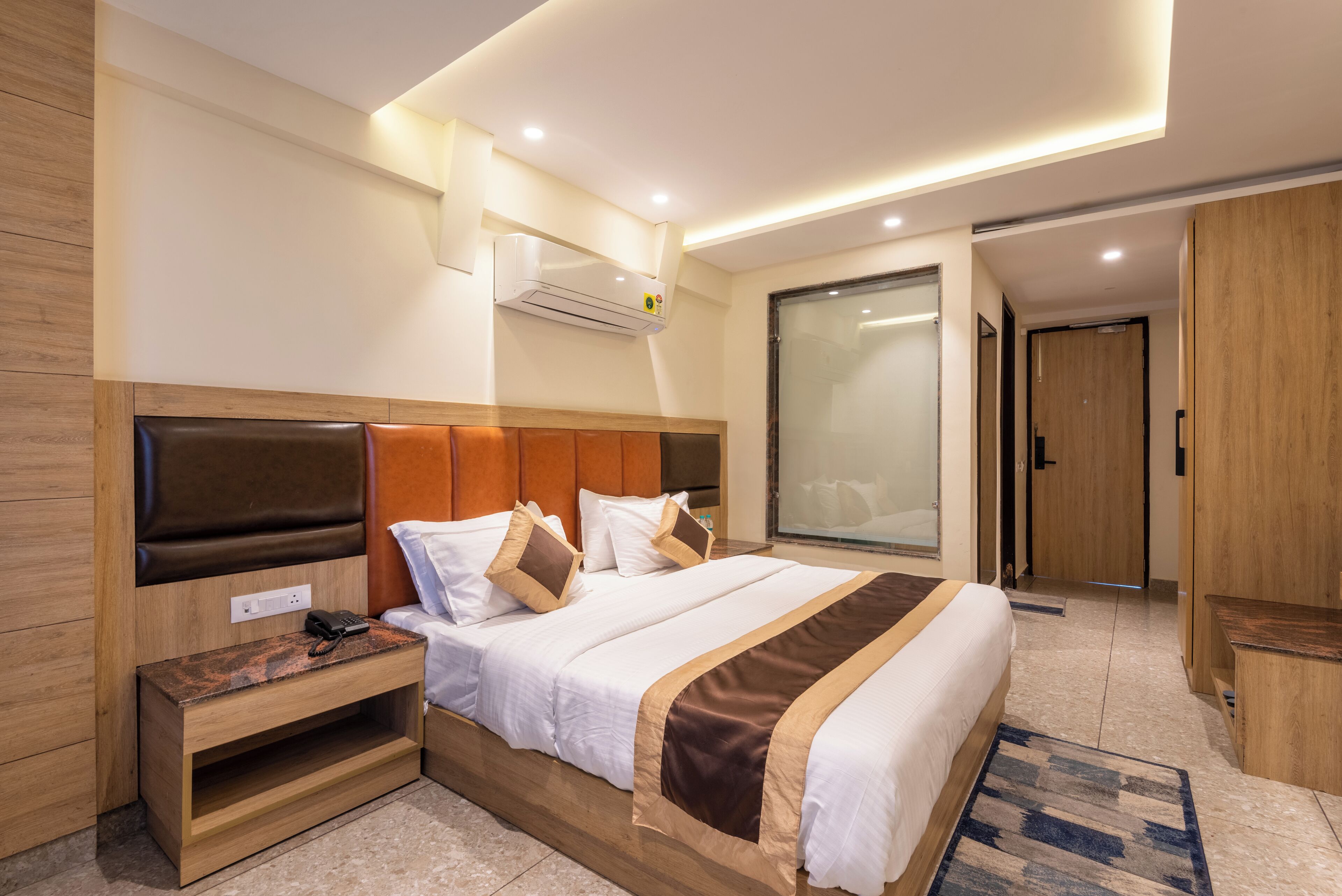 Una habitación de hotel moderna con una cama grande, cabecera de madera, mesitas de noche y aire acondicionado integrado.
