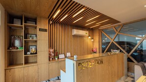 Un mostrador de recepción con detalles de madera y una superficie de vidrio, flanqueado por estanterías de madera con certificados y pequeñas plantas.