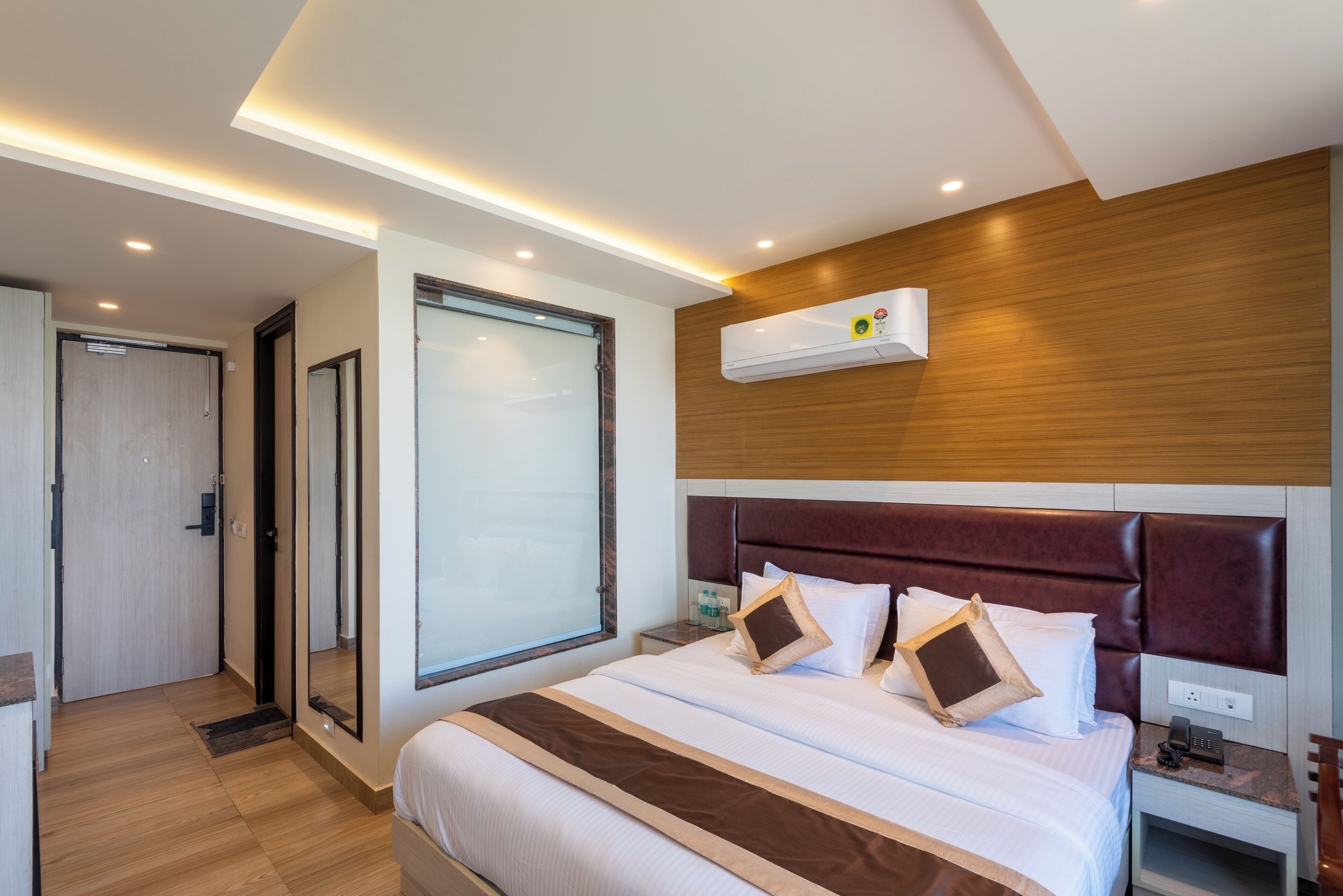 Una habitación de hotel moderna con una cama grande, un cabecero de madera, un equipo de aire acondicionado y una mesita de noche con un teléfono.