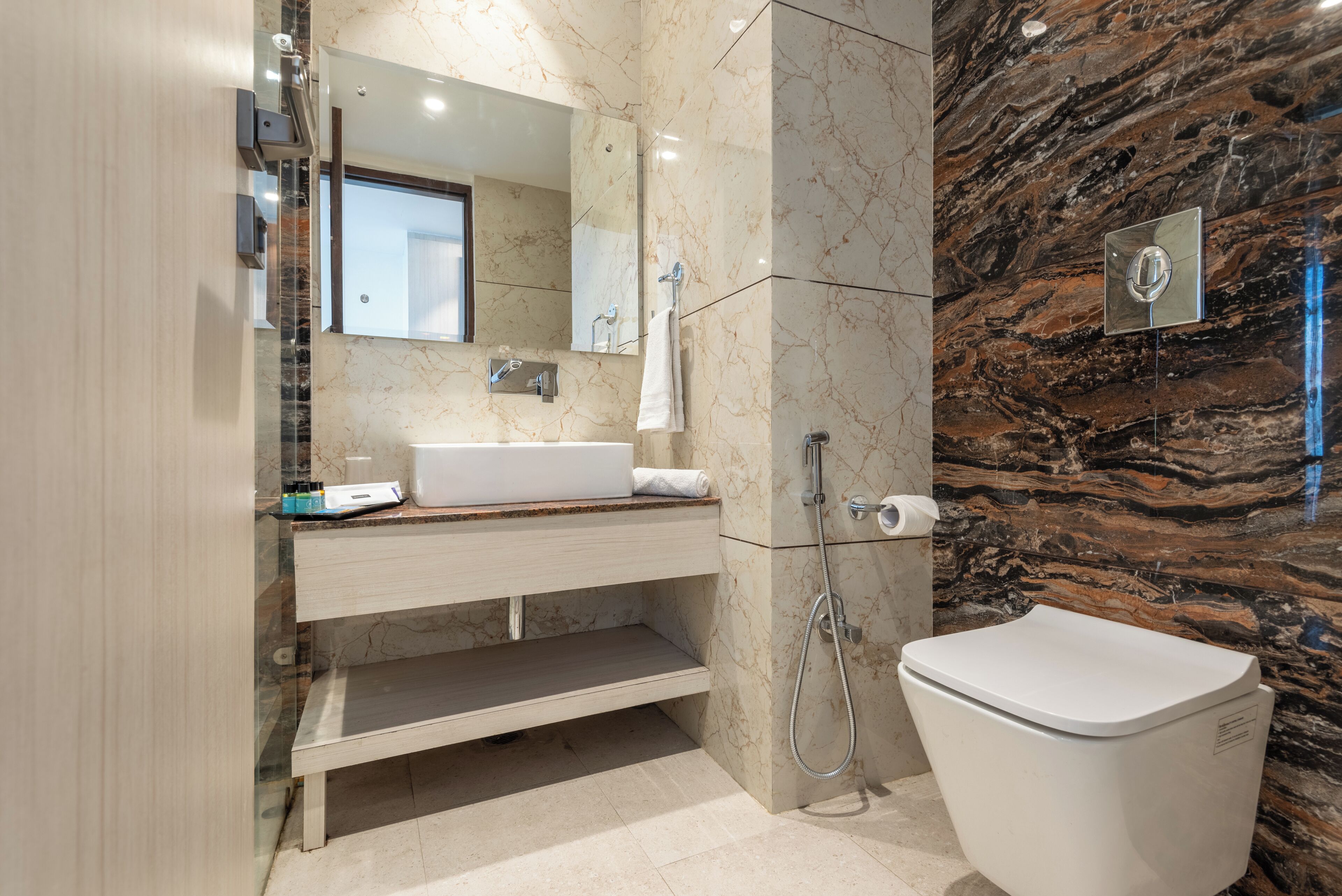 A modern bathroom with a marble wall, a white sink, and a toilet.