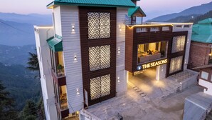 Un hotel de diseño moderno, con una entrada destacada que muestra el letrero "THE SEASONS". El edificio tiene una fachada singular con paneles estampados y una cubierta vegetal.
