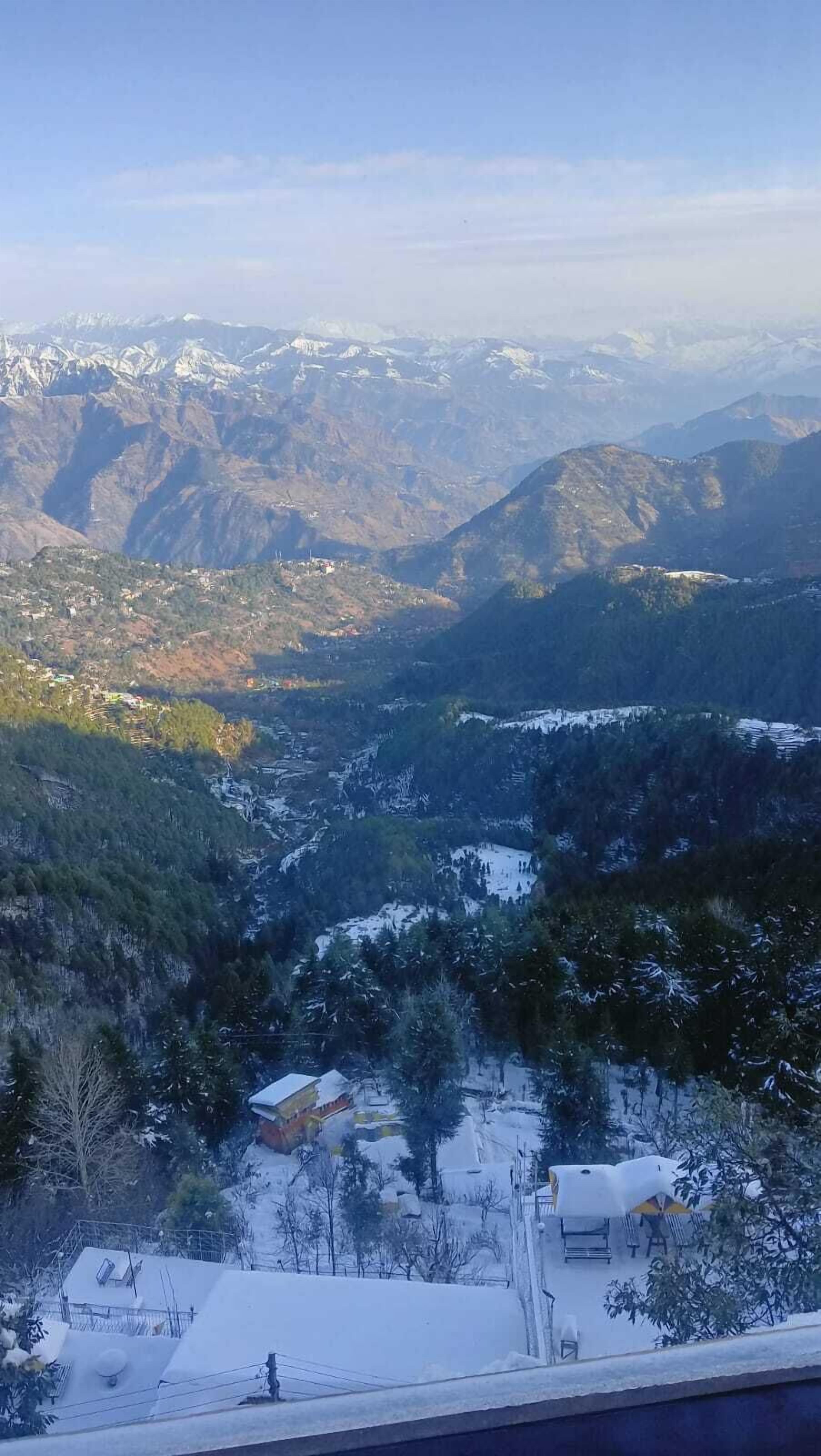 A mountainous landscape with snow-covered areas and a small settlement with buildings and trees.