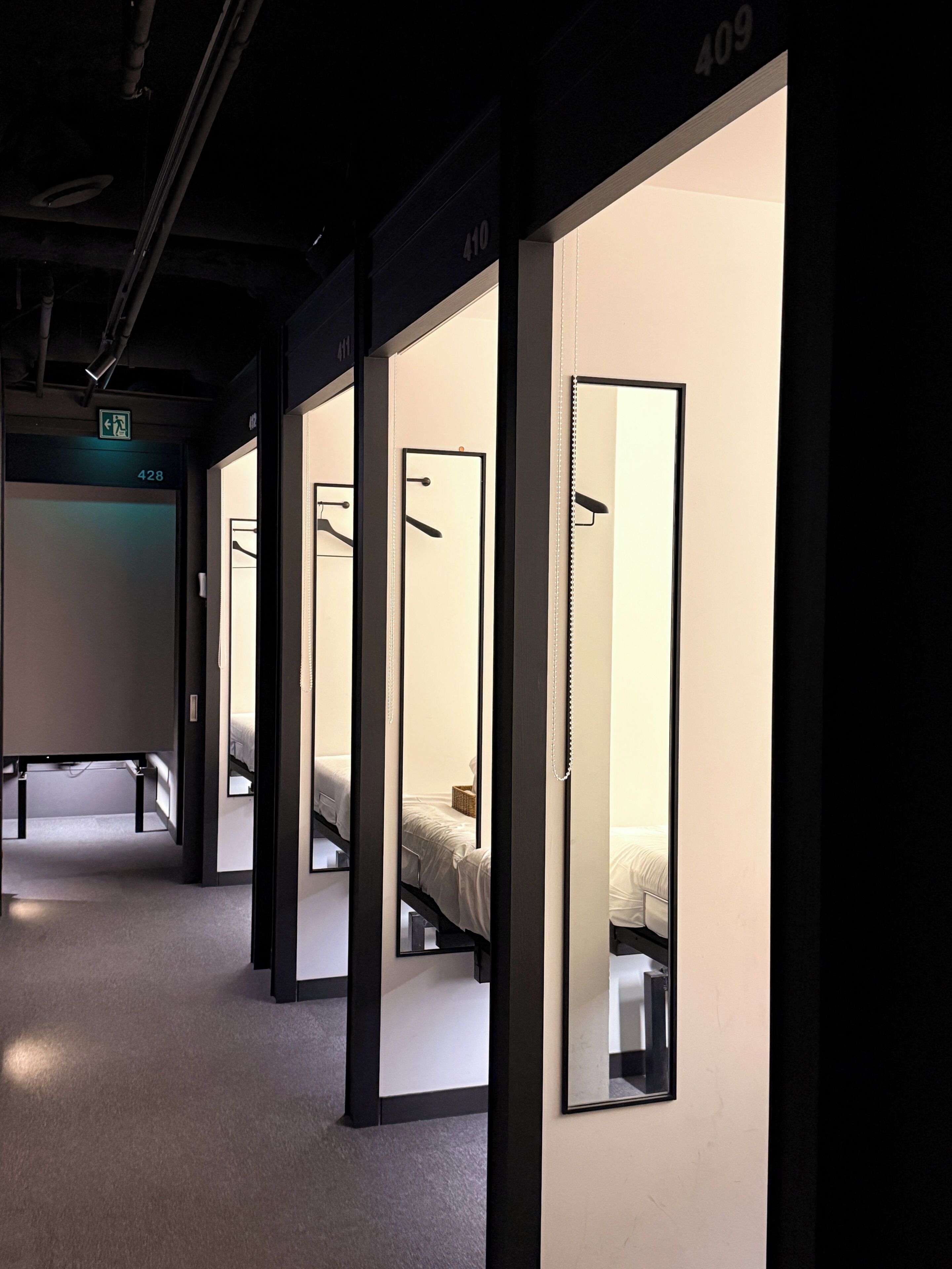 Een hotelgang met individuele kamers, elk met een bed en een kapstok.