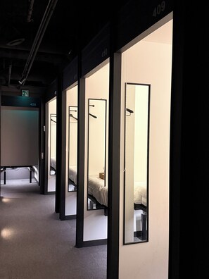 A hotel corridor with individual rooms, each with a bed and a hanging coat rack. - KOZAYO Hongdae Hostel (Seoul)
