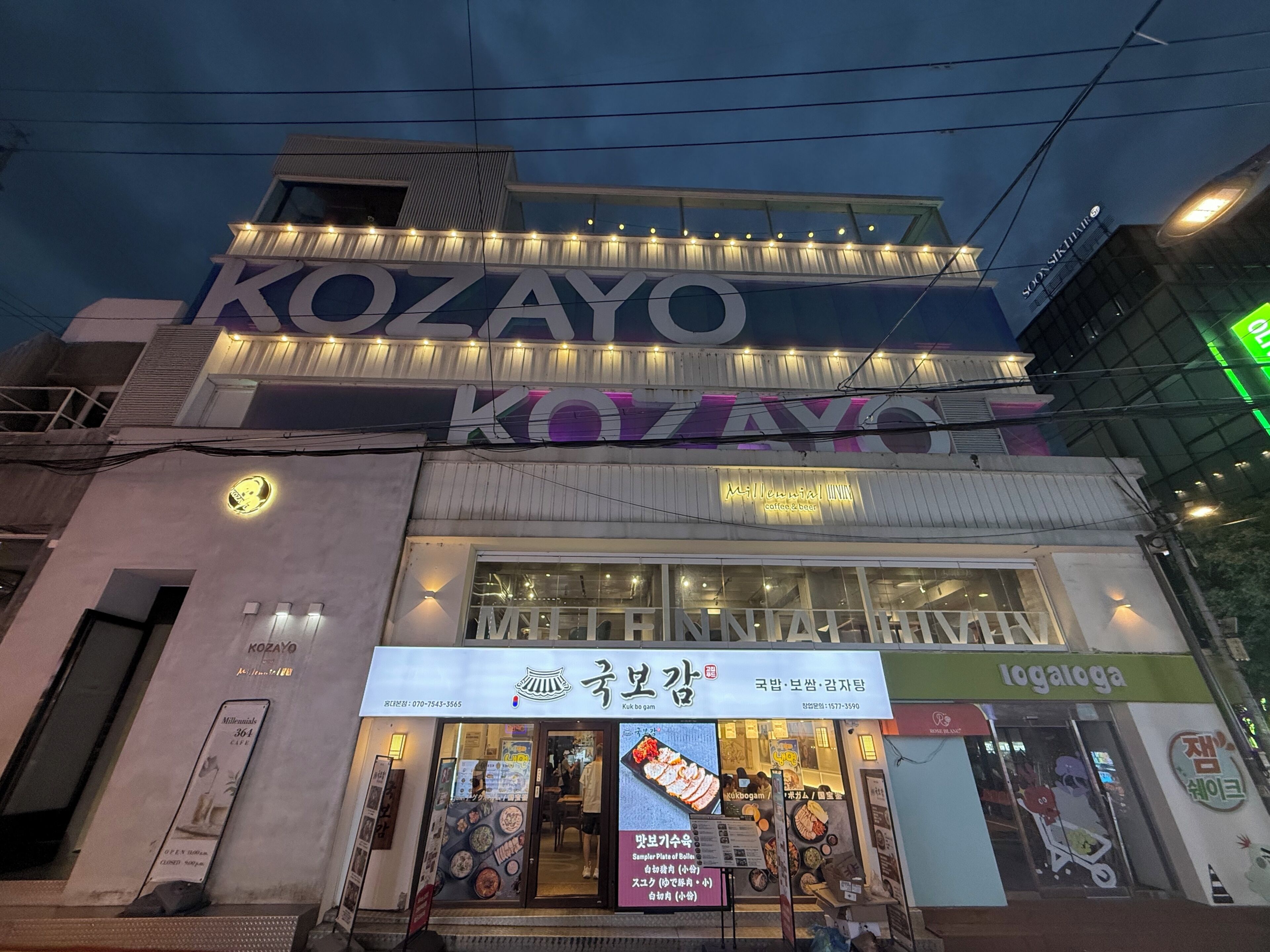 Een gebouw met borden voor 'KOZAYO' en 'Millennial Inn', met een restaurantsbord eronder.