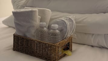 A neatly made bed with white bedding and pillows, a wicker basket with toiletries, and a wall socket.