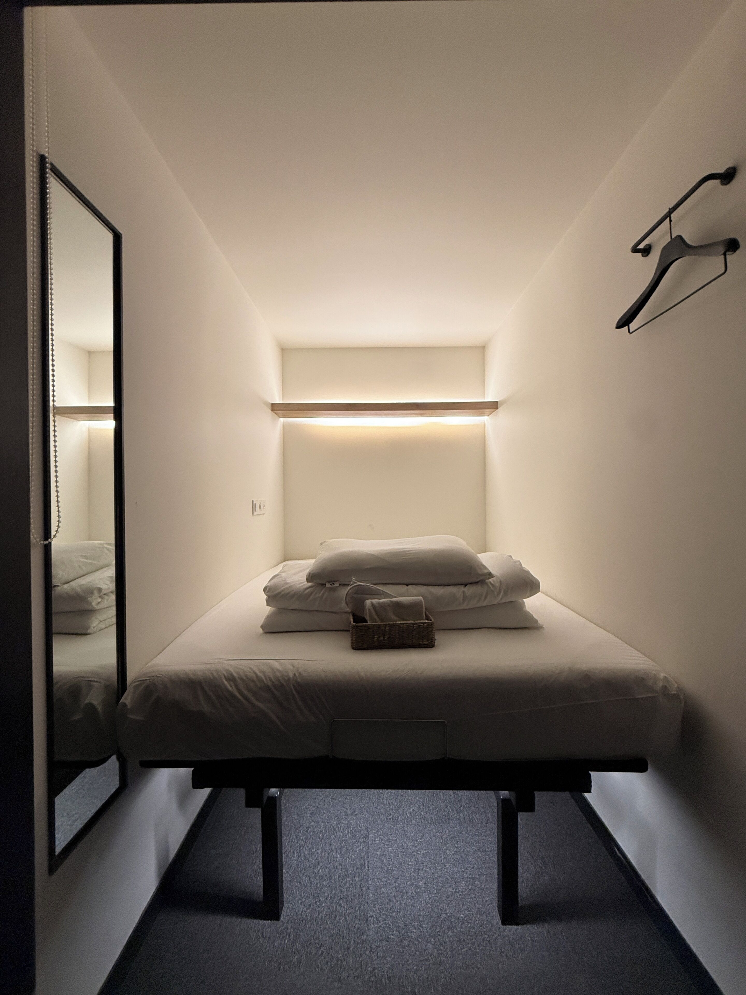 Un dormitorio pequeño y ordenado con una cama individual, una mesita de noche, una lámpara colgante y un espejo.