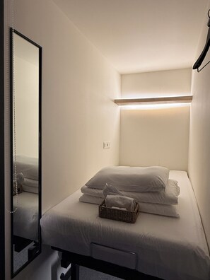 A small, neatly made bed with a headboard, a bedside table, and a mirror. - KOZAYO Hongdae Hostel (Seoul)