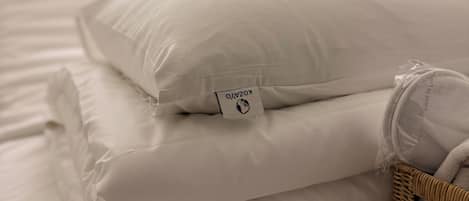 A neatly made bed with white bedding and a pillow with a visible brand tag.