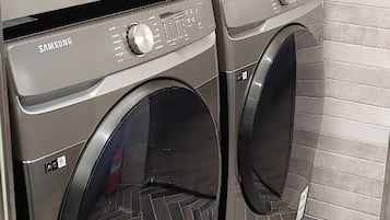 Een wasserette met twee Samsung voorladers wasmachines en drogers, betegelde muren en een visgraatvloer.