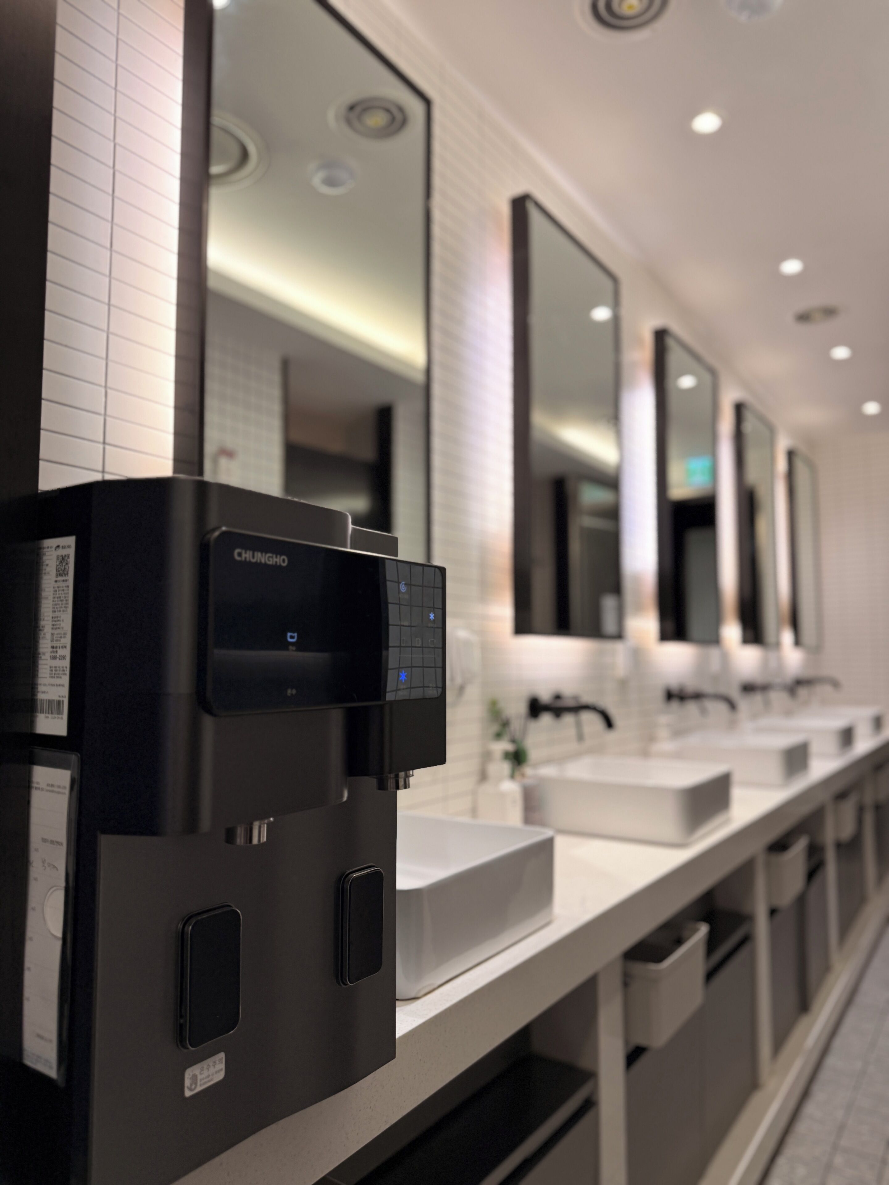 Un baño moderno con un grifo sin contacto negro, lavamanos blancos y espejos.