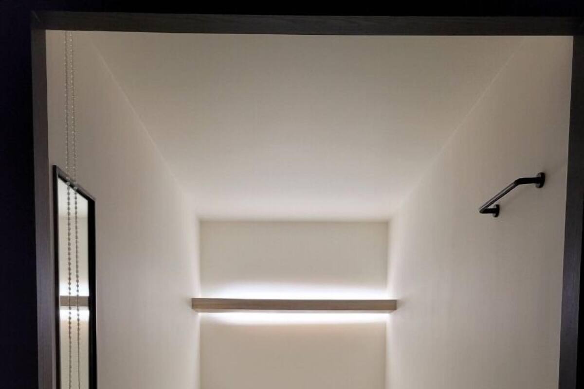 A narrow, single-bed room with a simple, clean design, featuring a bed with white bedding and a small bedside table.