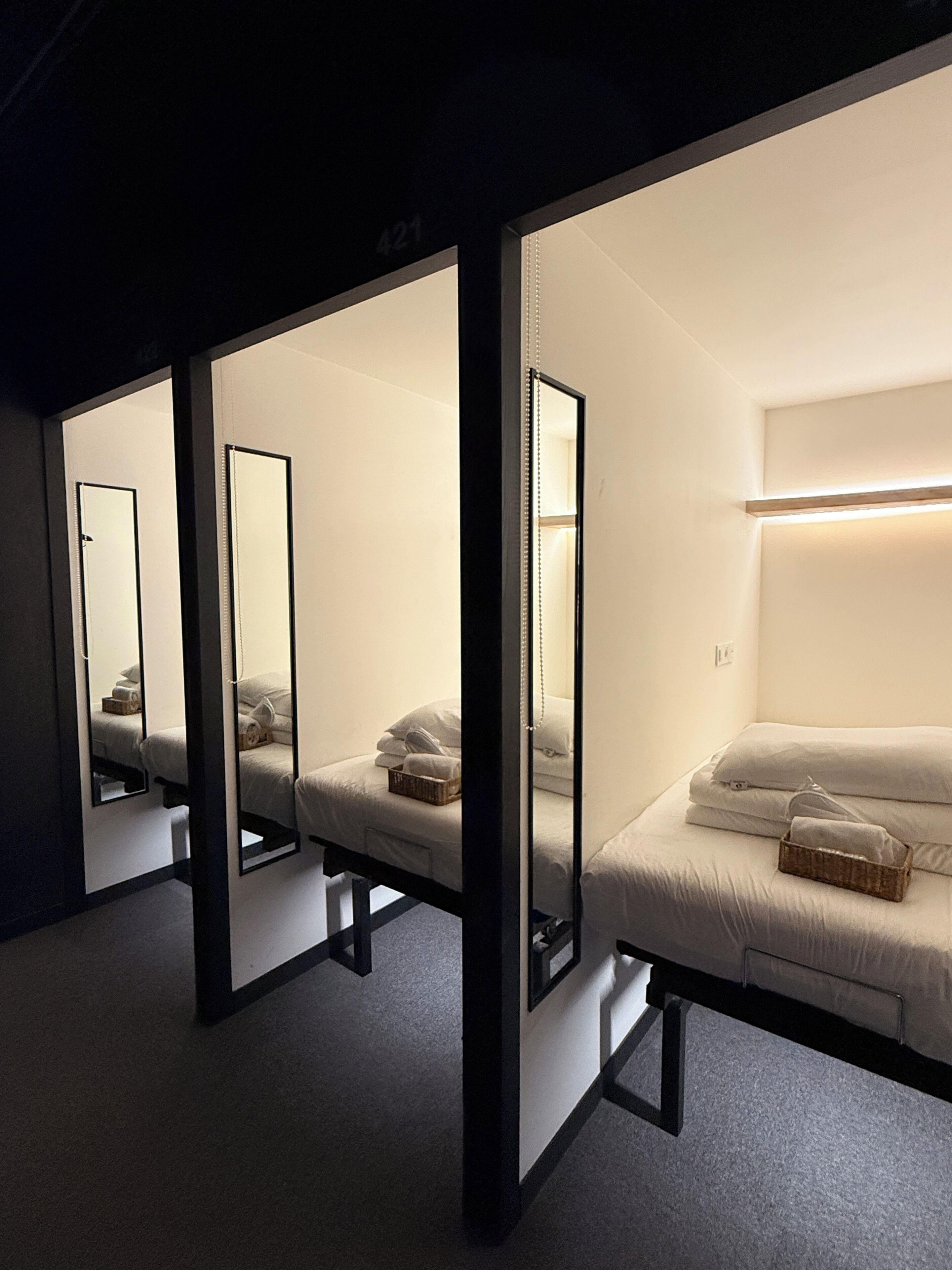 Een hotelkamer met een spiegelkast, een bed met witte lakens en een nachtkastje met een mand.