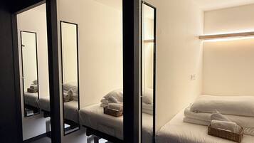 Een hotelkamer met een spiegelkast, een bed met witte lakens en een nachtkastje met een mand.
