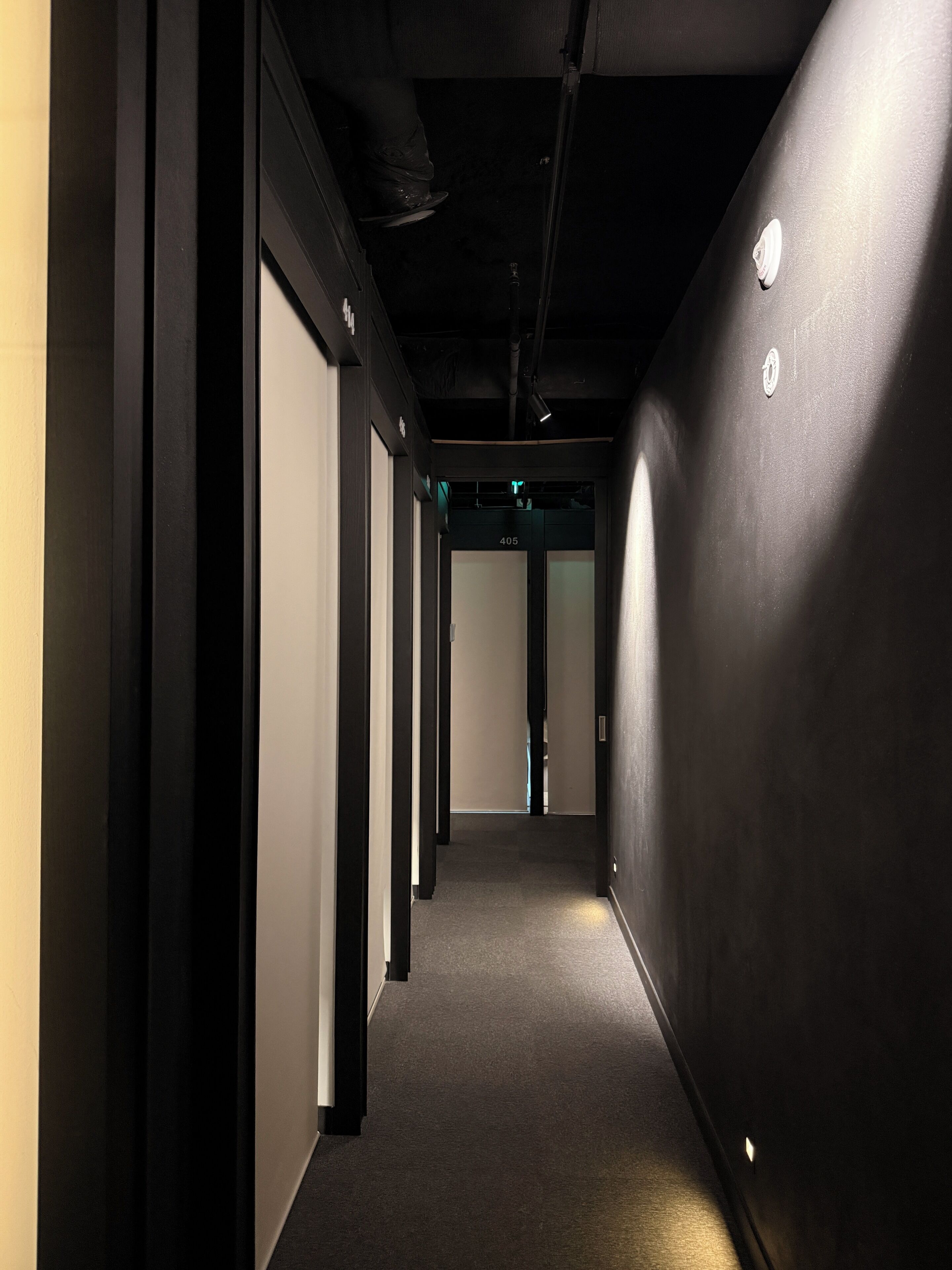 A corridor with a carpeted floor, black walls, and a door at the end.
