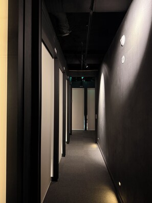 A corridor with a carpeted floor, black walls, and a door at the end. - KOZAYO Hongdae Hostel (Seoul)