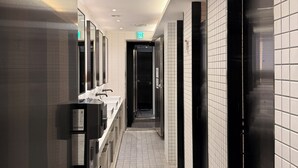 A modern bathroom with a long corridor, multiple sinks, and a visible exit sign. - KOZAYO Hongdae Hostel (Seoul)