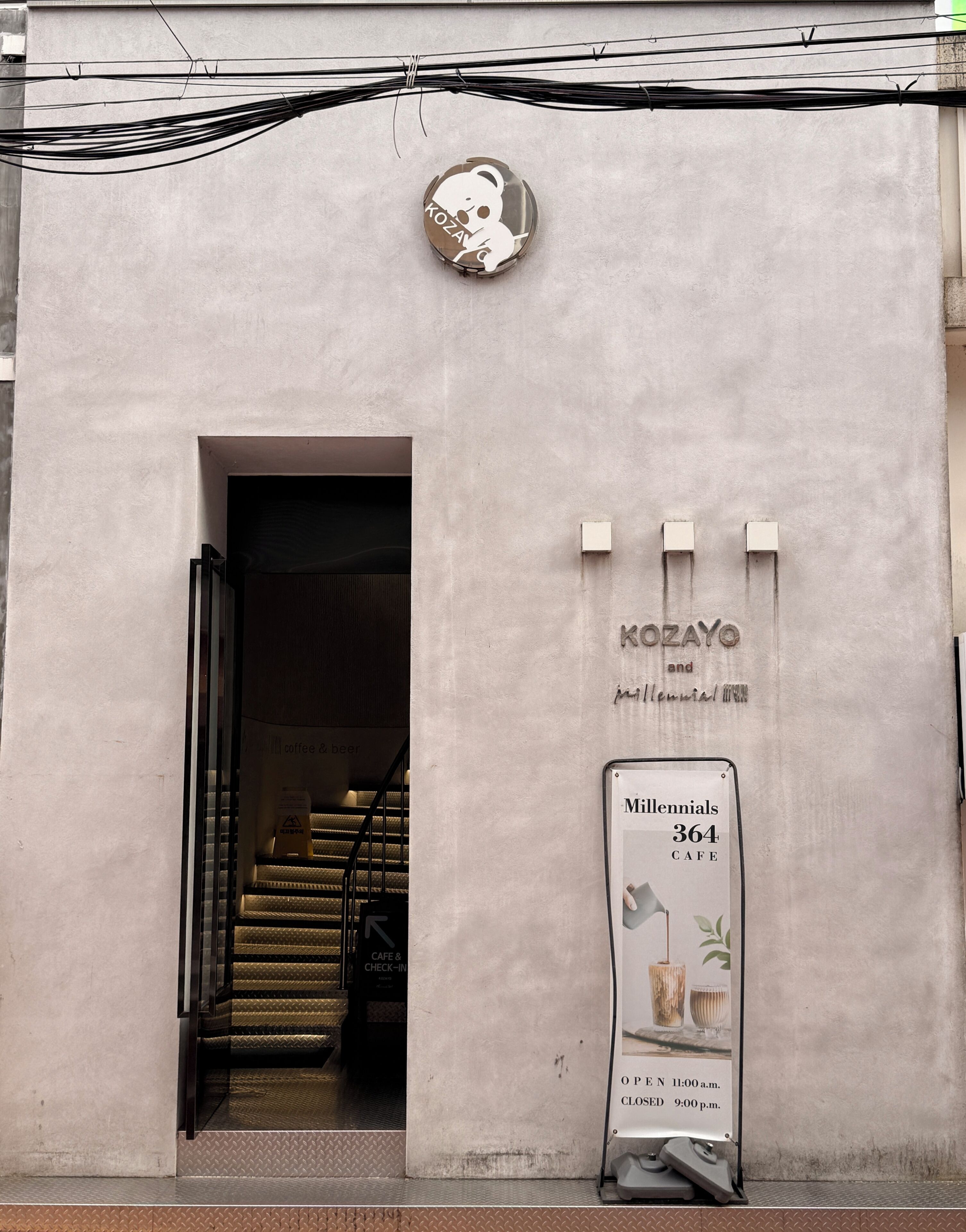 A building entrance with a sign for 'KOZAYO and millennials cafe' and a staircase leading inside.