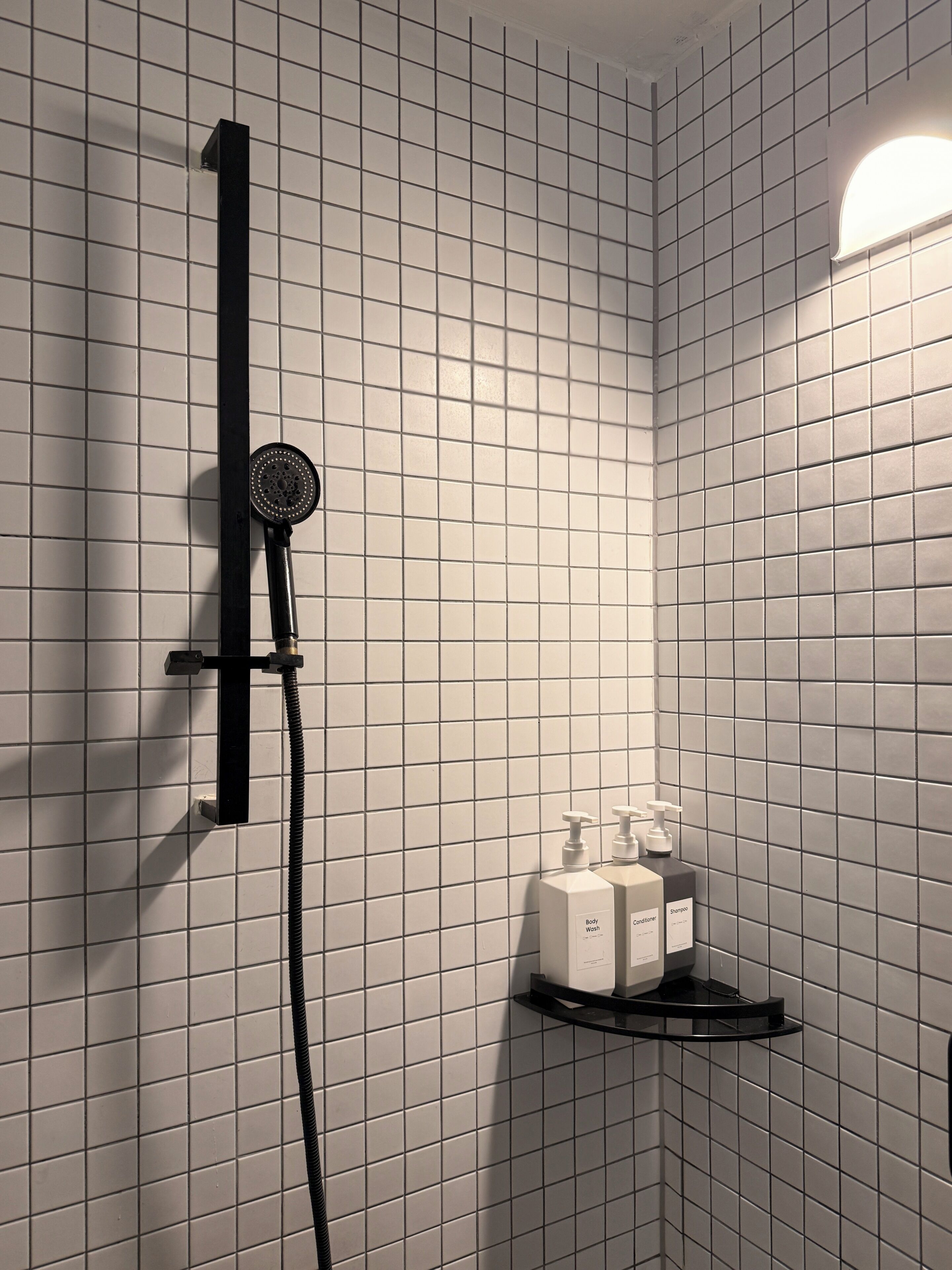 A bathroom with a shower, a towel rack, and a shelf with toiletries.