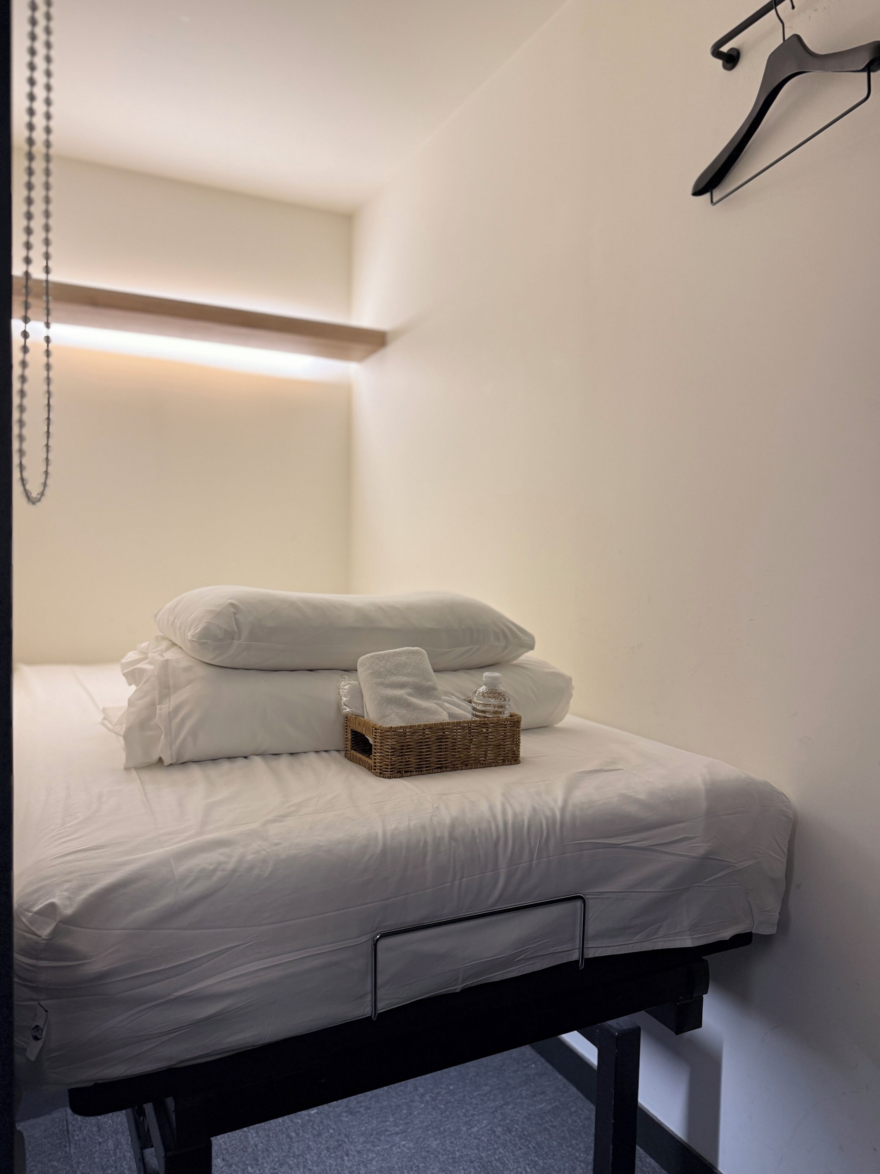 A neatly made bed with white linens, a wicker basket with towels, and a bottle of water on the bed.