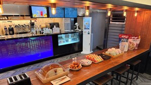 A bar area with a coffee machine, a food display, and a seating area with stools. - KOZAYO Hongdae Hostel (Seoul)