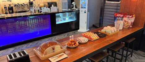 Zona de bar con máquina de café, mostrador de comida y área de estar con taburetes.