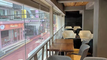 An interior view of a restaurant with wooden tables and chairs, a view of the street outside, and a ceiling with wooden panels and recessed lighting.