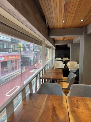 An interior view of a restaurant with wooden tables and chairs, a view of the street outside, and a ceiling with wooden panels and recessed lighting. - KOZAYO Hongdae Hostel (Seoul)