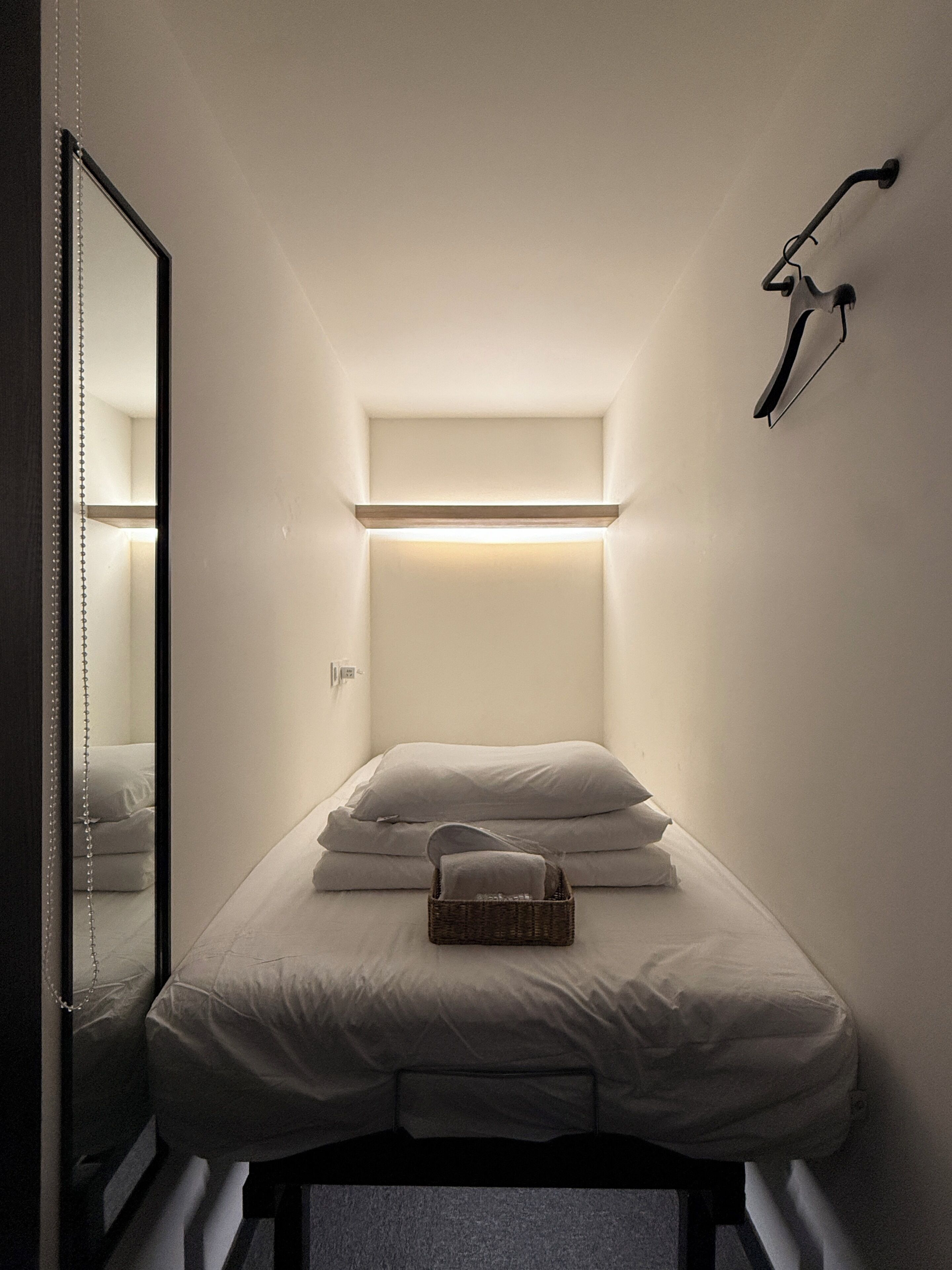 A small, narrow room with a bed, a hanging light fixture, and a mirror.