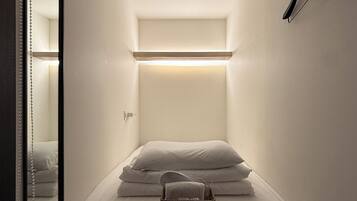 A small, narrow room with a bed, a hanging light fixture, and a mirror.