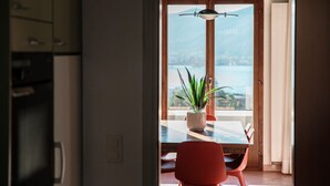 A dining area with a table and chairs, a potted plant, and a view of a body of water through a glass door. - Flat in the Gulf of Melano (Miralago) (Val Mara)