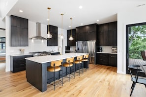 A modern kitchen with a central island, bar stools, dark cabinetry, and a stainless steel refrigerator. - Moonlight Manor - Private Pool, Theatre Room & More! (Sunrise Beach)