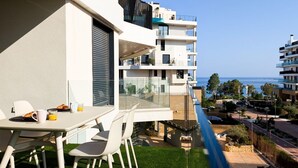 Ein Balkon mit Tisch und Stühlen, der auf einen Wohnbereich und das Meer blickt.