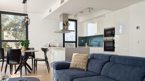 Ein modernes Wohnzimmer mit einem dunkelblauen Sofa, einem runden Couchtisch und einem Essbereich mit schwarzen Stühlen und einem kleinen Tisch.