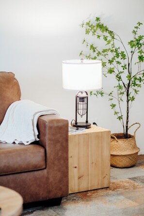 En brun lædersofa med et hvidt plaide, et træsidebord med en lampe, og en potteplante.