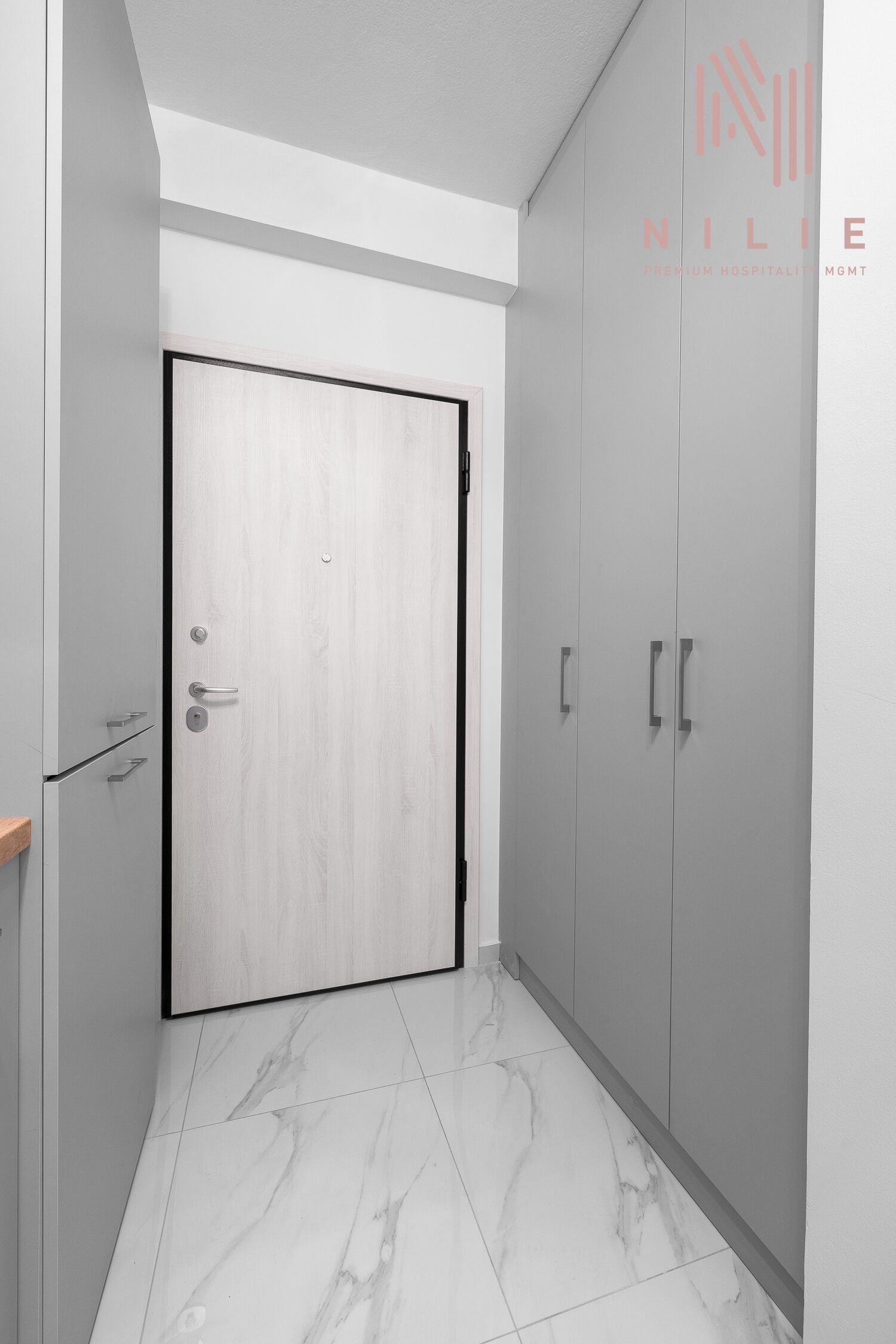 A hallway with a wooden door, grey cabinets, and marble flooring.