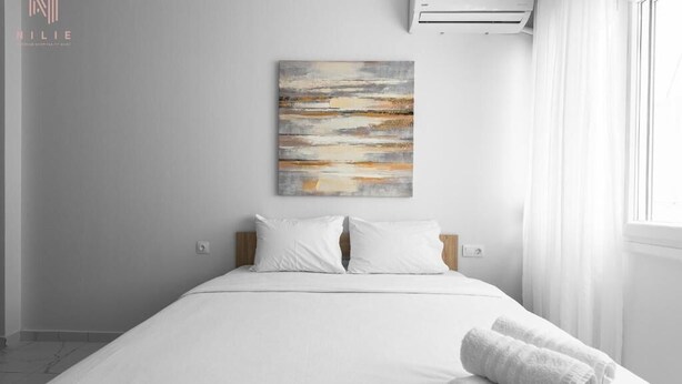 Una camera d'albergo moderna con un letto grande, biancheria bianca, un quadro appeso e un condizionatore d'aria.