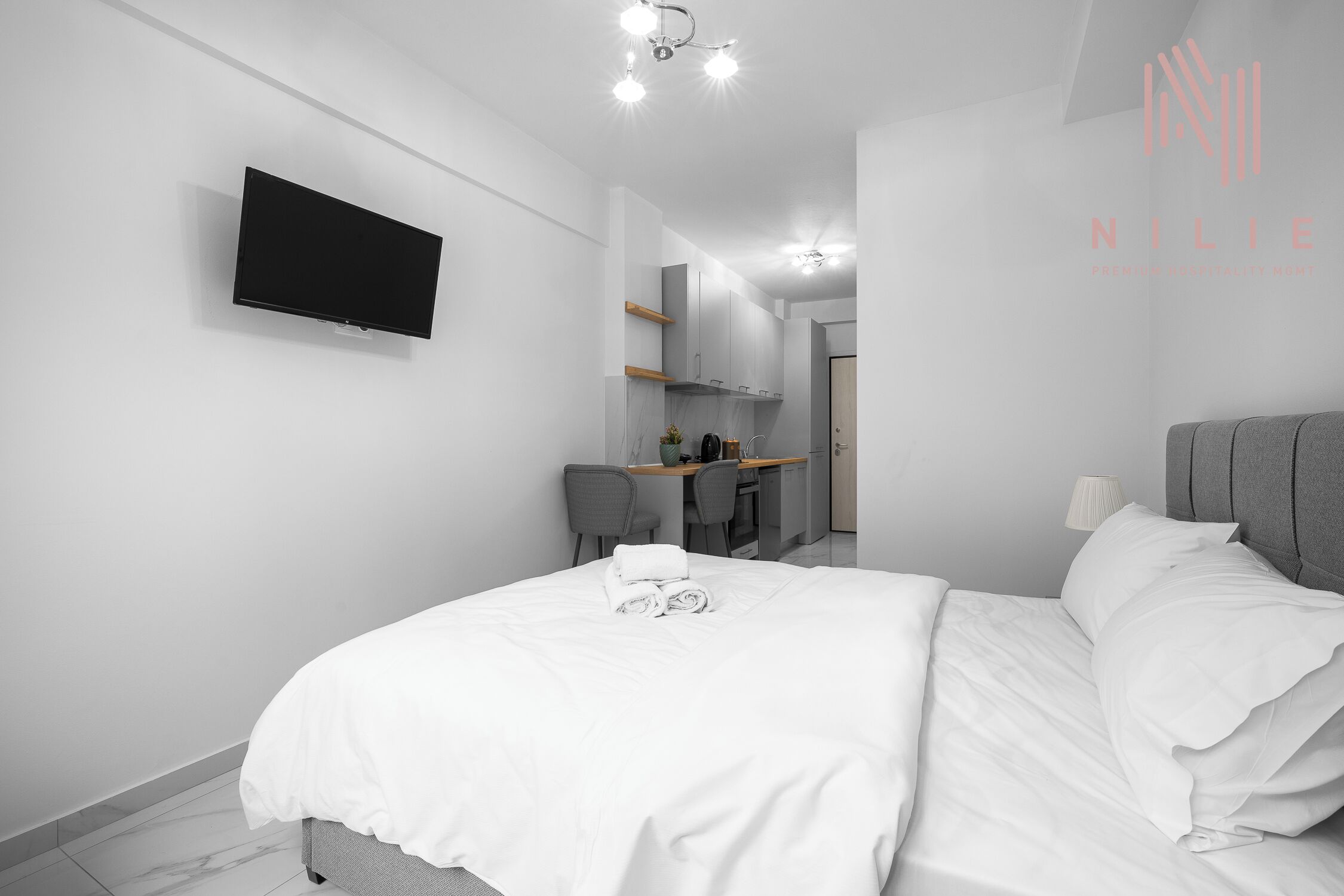 Una habitación de hotel moderna con un televisor de pantalla plana montado en la pared, un escritorio con una silla y una cama con toallas ordenadas.