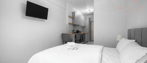 Una habitación de hotel moderna con un televisor de pantalla plana montado en la pared, un escritorio con una silla y una cama con toallas ordenadas.