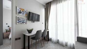 Habitación de hotel moderna con una televisión de pantalla plana montada en la pared, una mesita con dos sillas y un ventanal con cortinas de gasa.