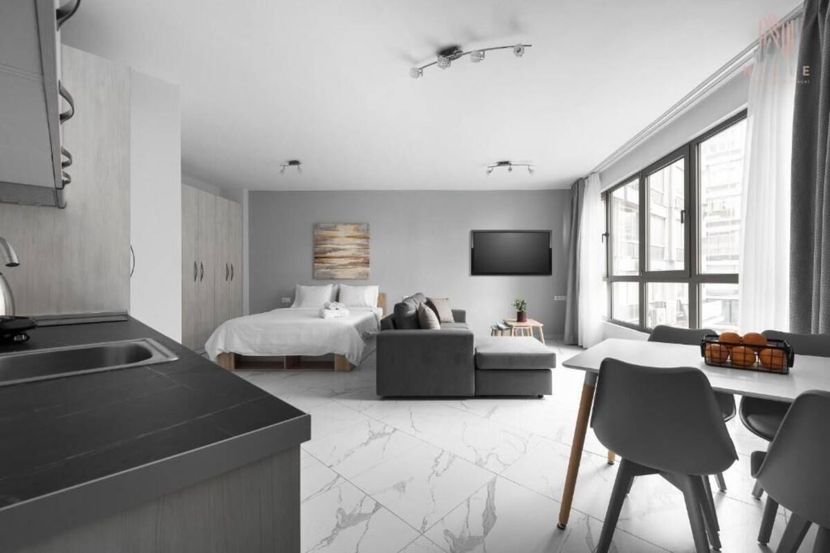 A modern hotel room with a kitchen, a dining area, a bed, and a TV.