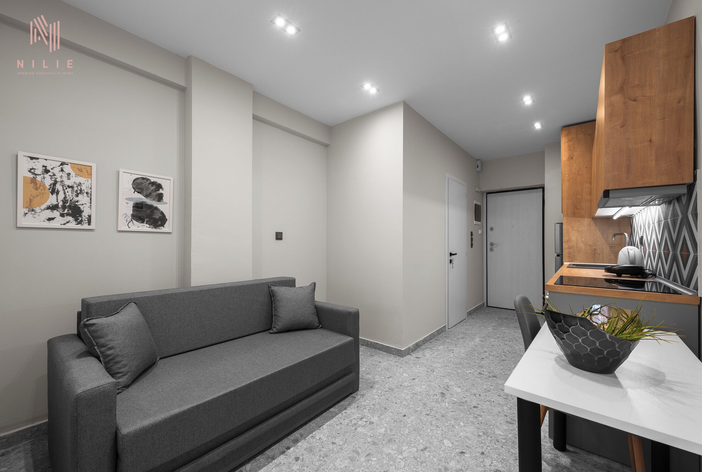 Una sala de estar moderna con un sofá gris, una mesa de comedor con un cuenco geométrico como centro de mesa y dos cuadros abstractos en la pared.