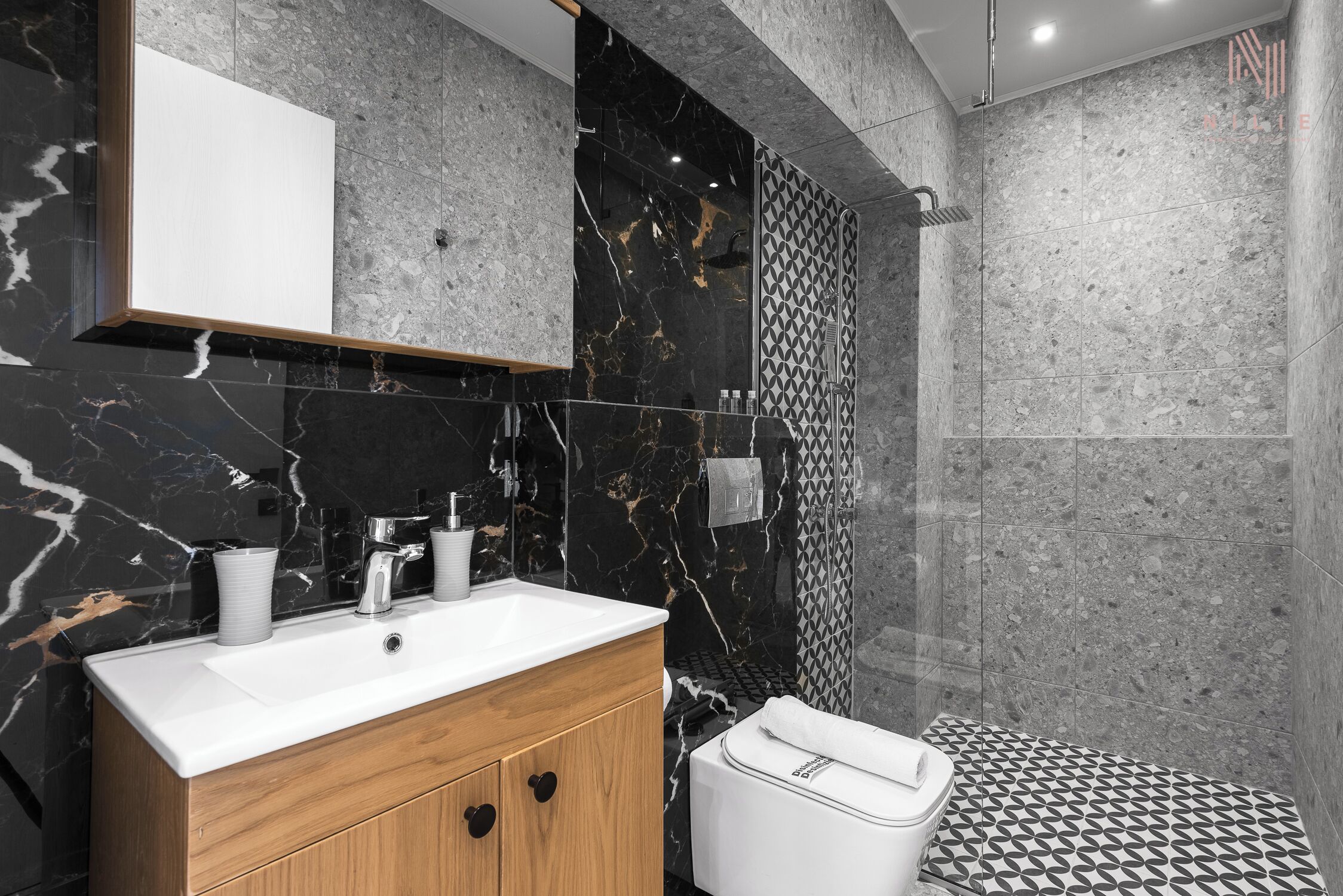 Ein modernes Badezimmer mit Marmorwaschbecken, Holzschrank und Dusche mit gemusterten Fliesen.