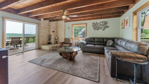 A spacious living room with a stone wall, a leather sofa, a glass coffee table, and a ceiling fan. - Branson's Crystal Cabin (Omaha)